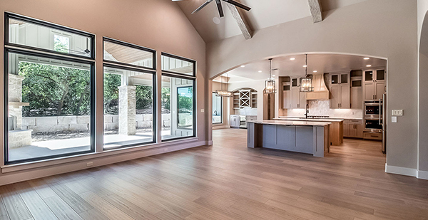 Open-concept kitchen and living space featuring custom cabinetry, large picture windows, designer lighting, and natural light throughout.