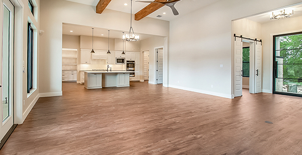 Spacious open living area with vaulted ceilings, exposed wood beams, luxury vinyl plank flooring, and custom kitchen