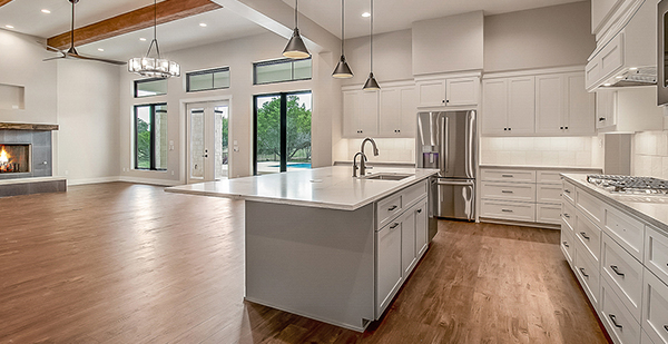 Open-concept custom home kitchen with oversized island, white cabinetry, quartz countertops, and seamless living area connection